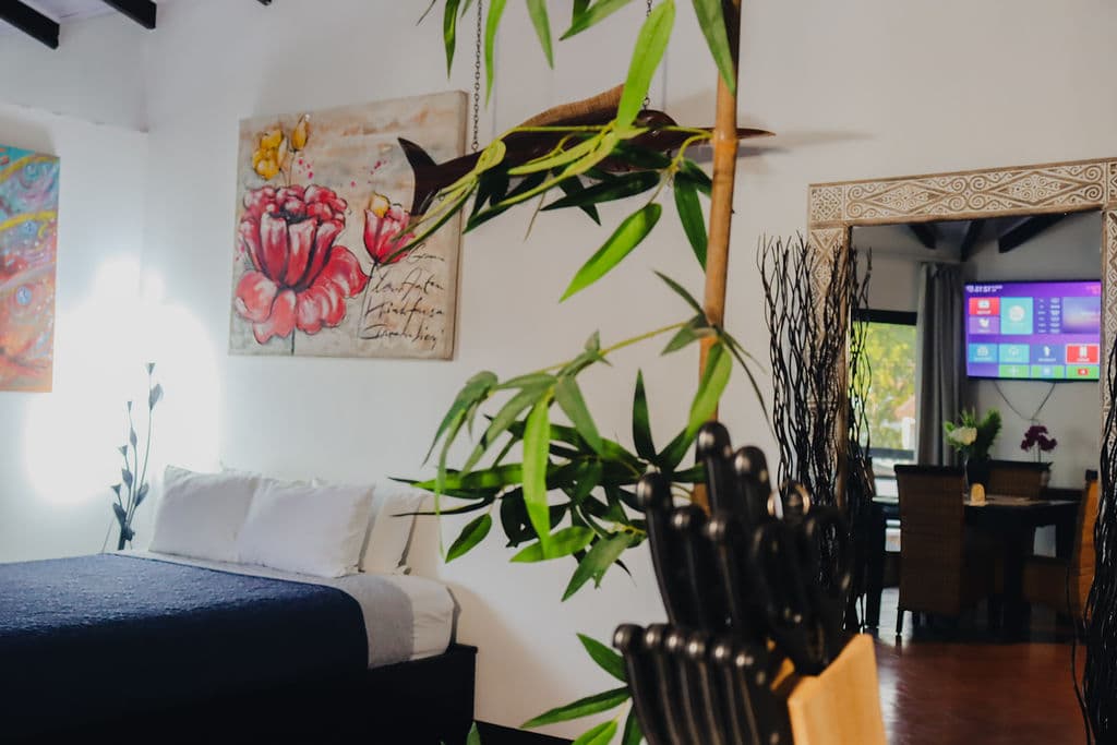 Villa bedroom with a bed, floral painting and a view to the dining area with TV