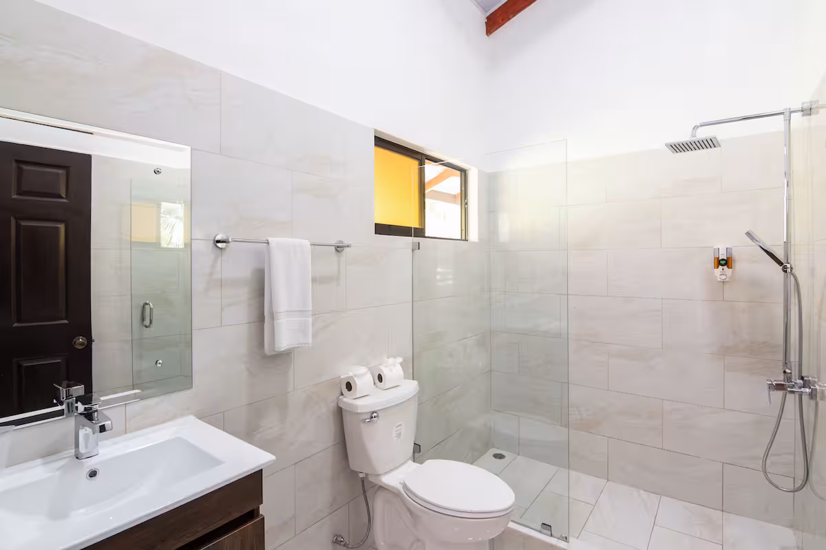 Baño de azulejo blanco con ducha de vidrio tipo lluvia
