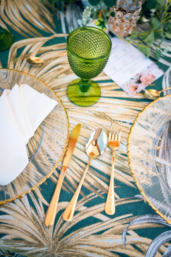 Detalle del montaje de mesa: cubertería dorada, cristalería y mantelería tropical