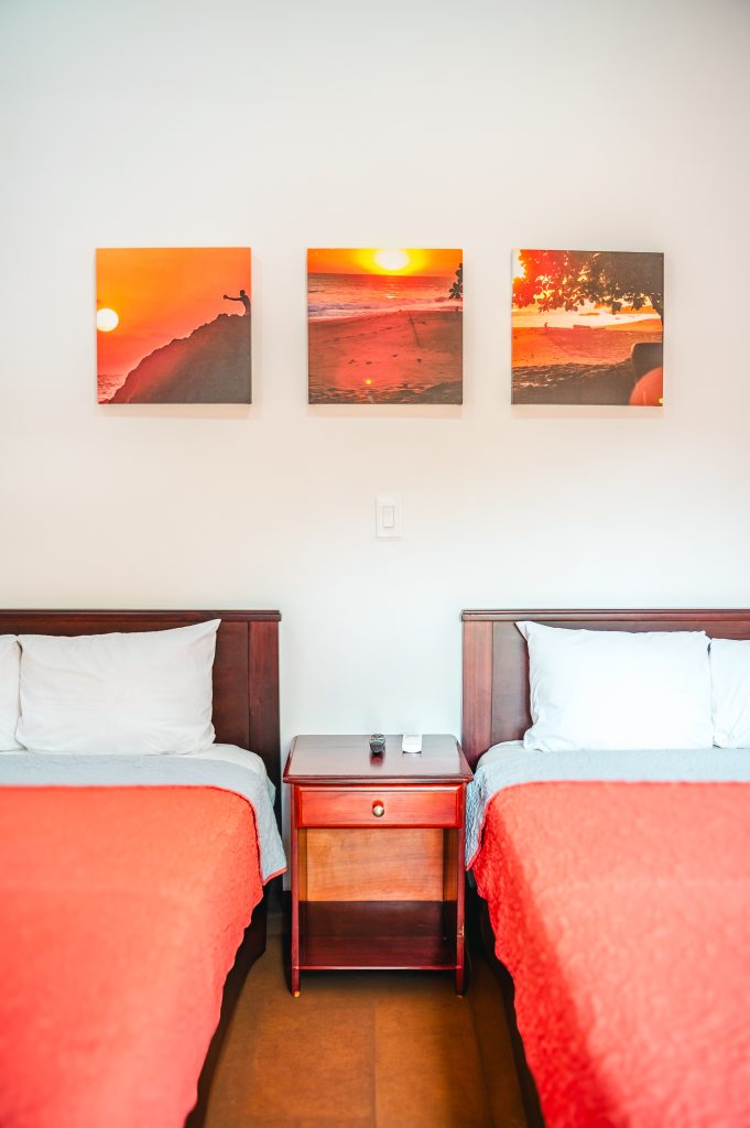 Two beds with wooden headboards beneath a triptych of sunset photographs